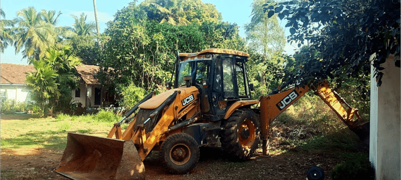 A yellow JCB backhoe loader parked on the property during initial ground clearing and site preparation.